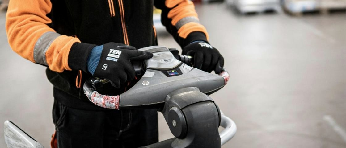 Warehouse worker in high visibility clothing operating a powered pallet truck
